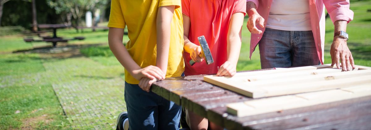 Children using a hammer at a workbench while an adult steadies the wood