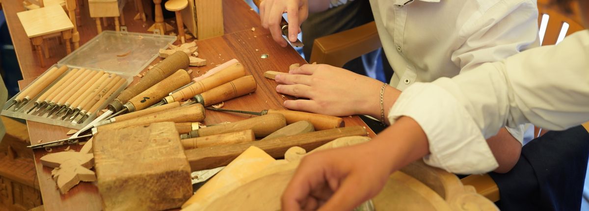 Wood carving chisels and a mallet in use at a bench, with small finished wooden pieces nearby